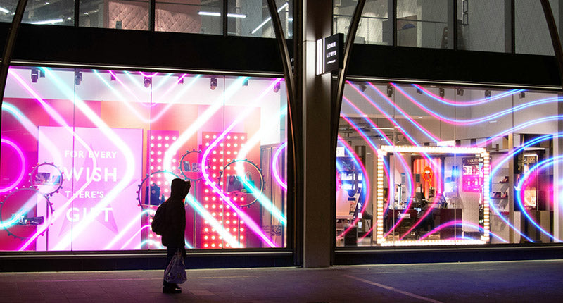 Transparant LED display op winkelpui bij avond met kleurrijke neon lichteffecten — LED film installatie retail